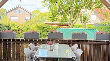 An outdoor patio with a table and chairs, a wooden deck, and a view of a house and trees.