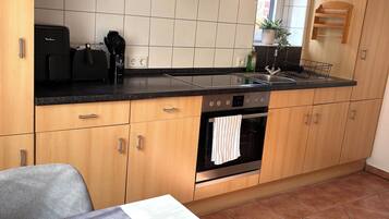A kitchen with wooden cabinets, a black countertop, a built-in oven, and a dining area with a table and a bowl of fruit.