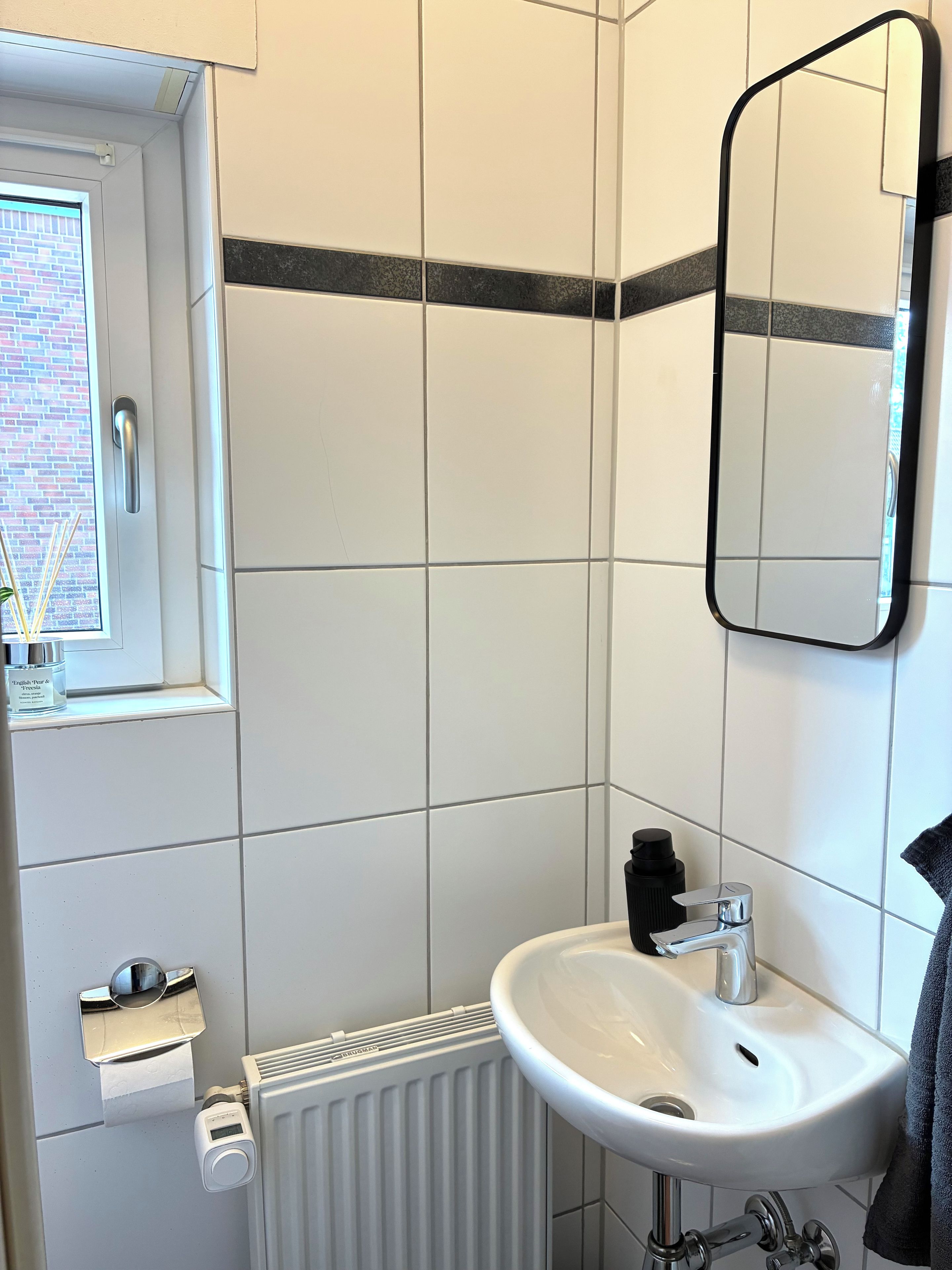 Une salle de bain avec un lavabo blanc, un miroir, une fenêtre et un porte-serviettes.