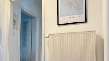 A hallway with a framed artwork above a radiator, a door with a nameplate, and a tiled floor.