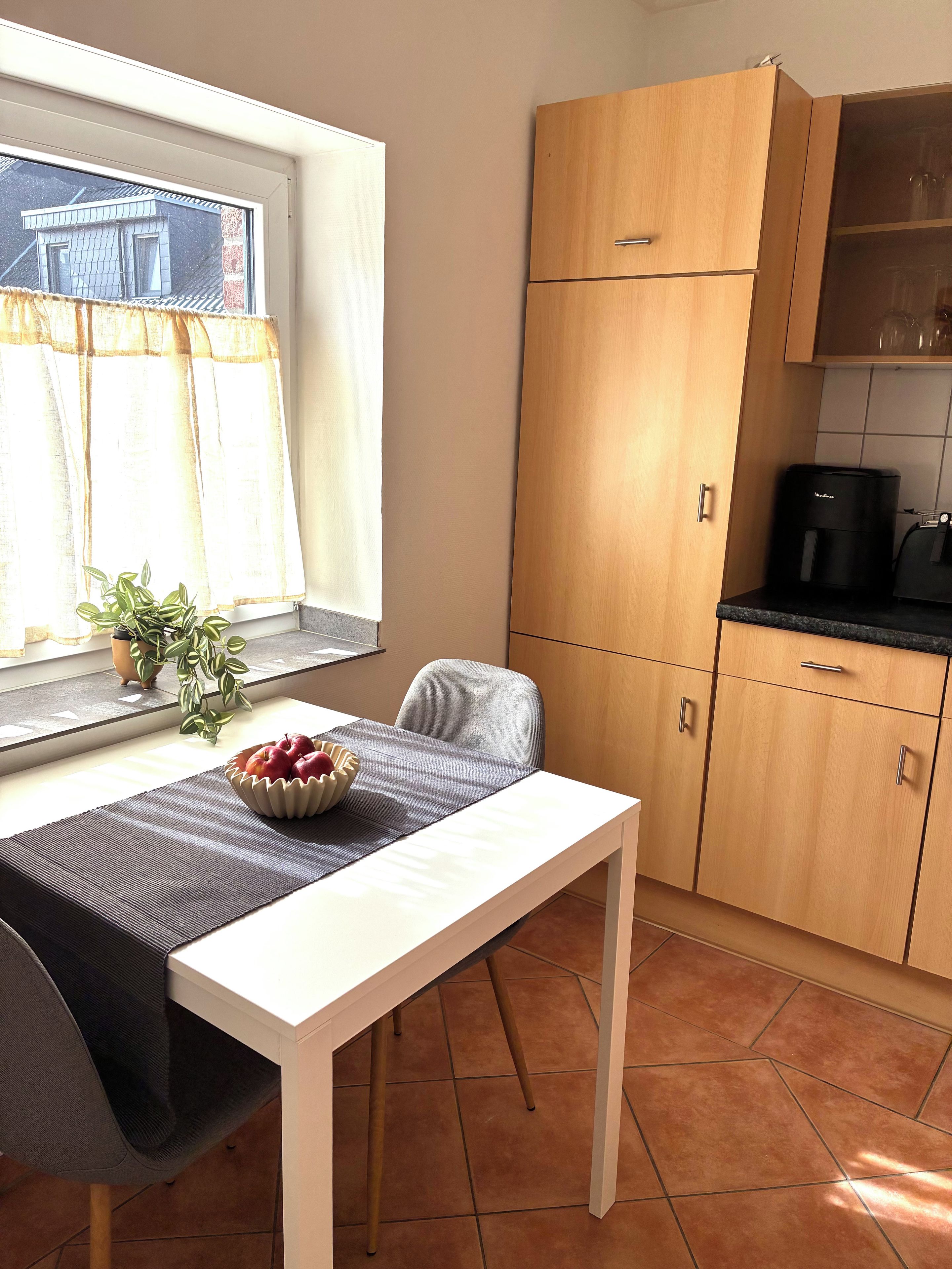 Una cocina pequeña con una mesa de comedor, una cafetera y un ventanal con cortinas.