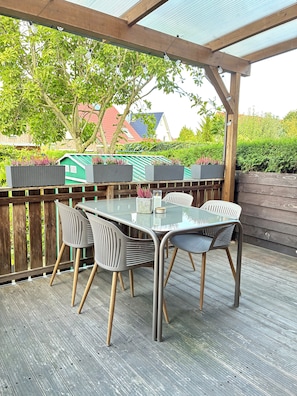 Un patio al aire libre con una mesa y sillas de vidrio, rodeado por una terraza de madera y una valla de madera.
