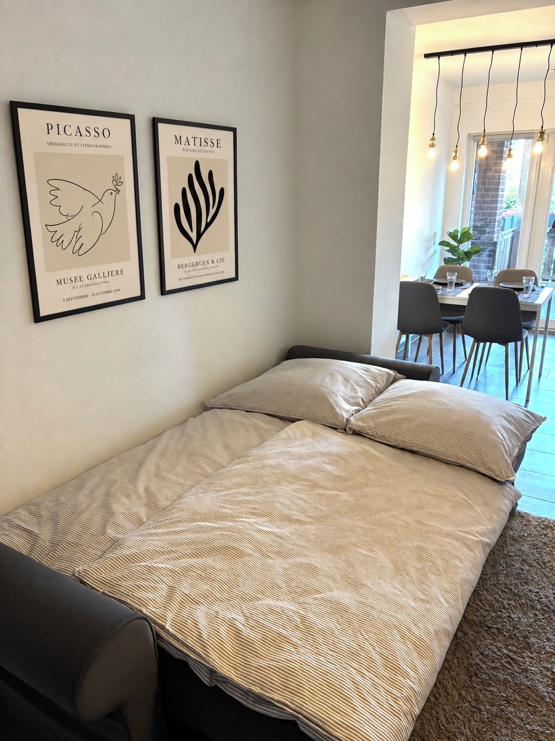 A room with a bed, a dining area with chairs, and two framed artworks on the wall.