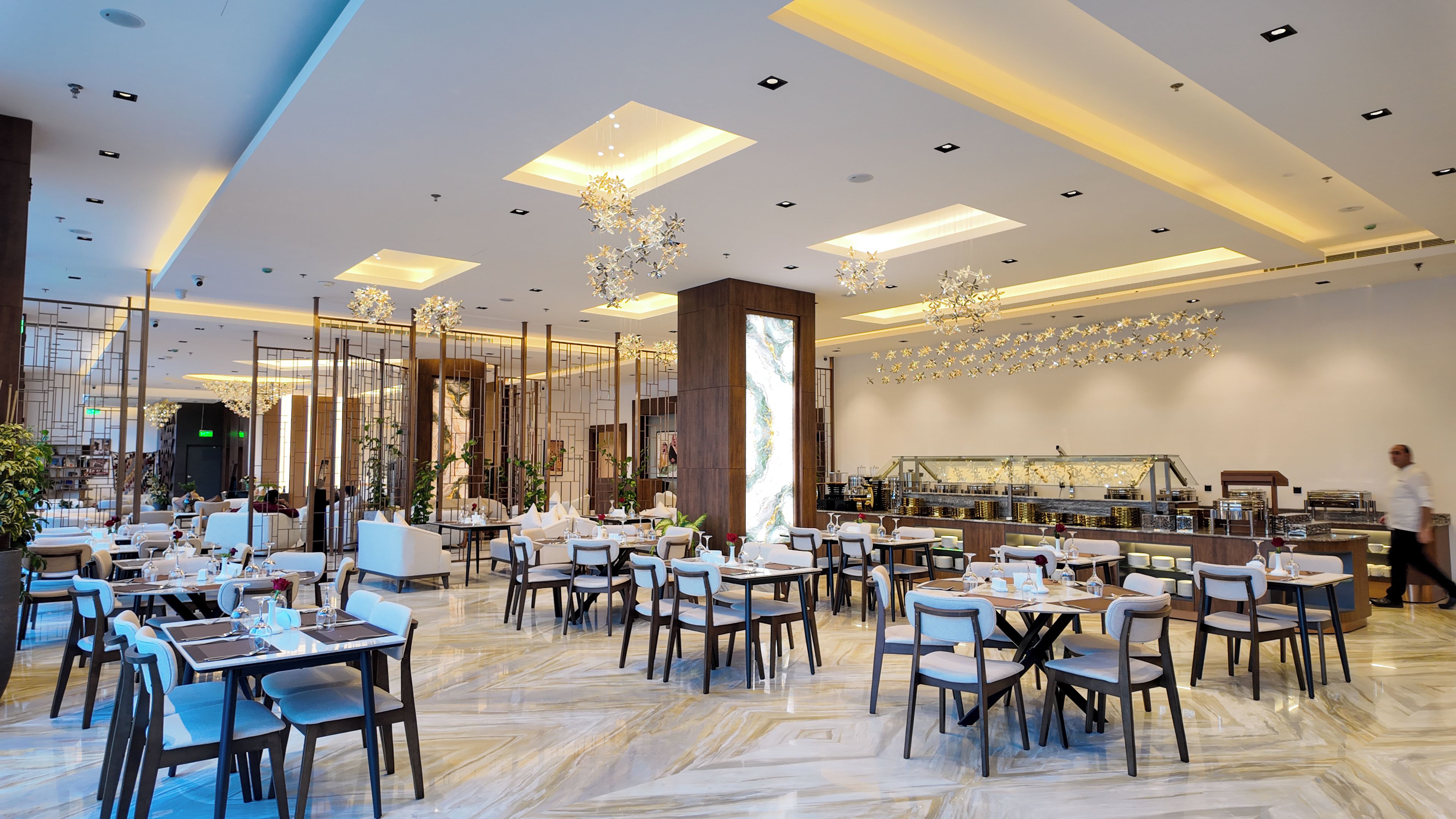 Un'ampia sala da pranzo con diversi tavoli e sedie, un'imponente colonna decorativa e un moderno lampadario.