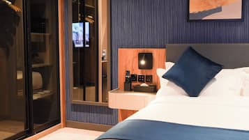 A hotel room with a bed, a nightstand with a remote control, a television, and a sliding door closet.