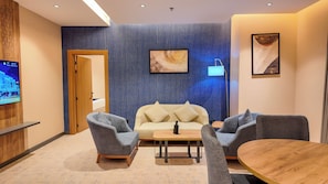 Una habitación moderna con sofá, dos sillones, una mesa de madera y un televisor en la pared.