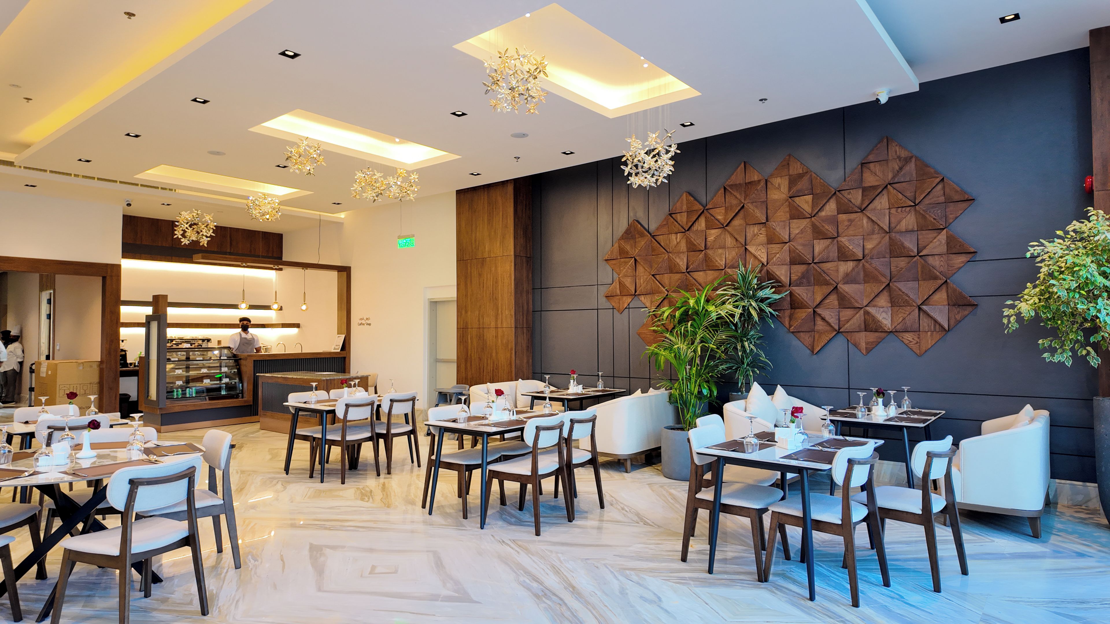 A modern dining area with tables and chairs, a coffee bar, and decorative wall panels.