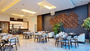 A modern dining area with tables and chairs, a coffee bar, and decorative wall panels. - LEMARS HOTEL (Riyadh)