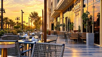 An outdoor dining area with wicker chairs and tables, palm trees, and a building with a sign that reads 'Café Lemars Restaurant & Café.'