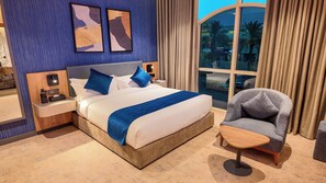 A hotel room with a large bed, a bedside table with a remote control, a chair, and a window with curtains.