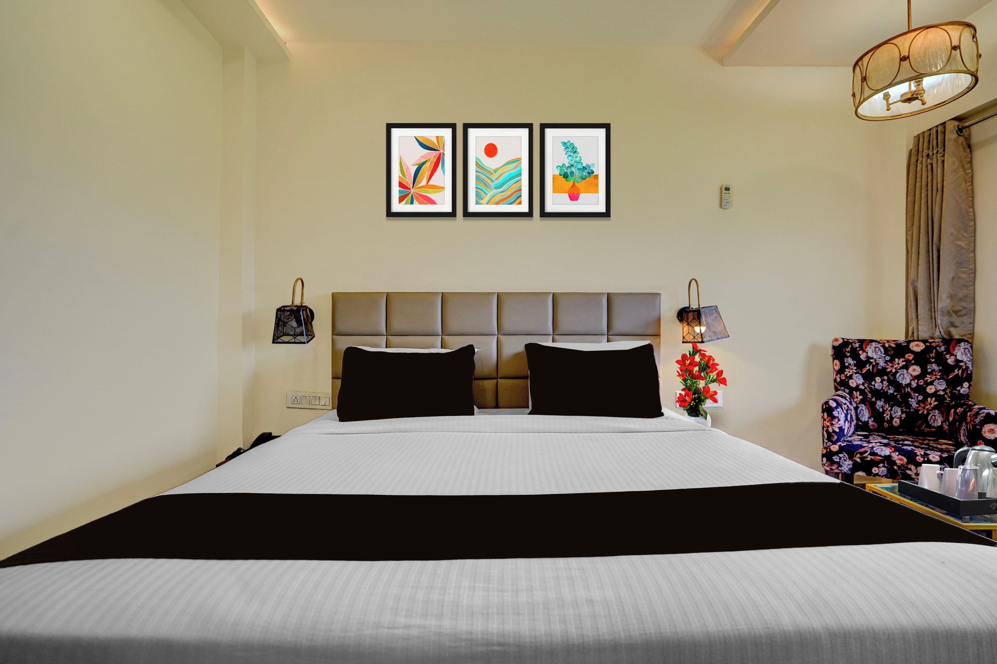 A hotel room with a large bed, a headboard, a nightstand, a chair, and three framed artworks on the wall.