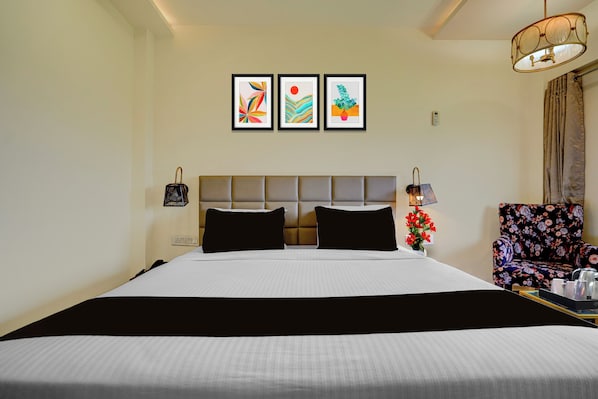 Habitación de hotel con una cama grande, cabecera, mesita de noche, una silla y tres cuadros en la pared.