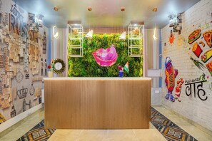 A reception desk with a green wall backdrop, surrounded by a wall with various country names and a mural of food items.