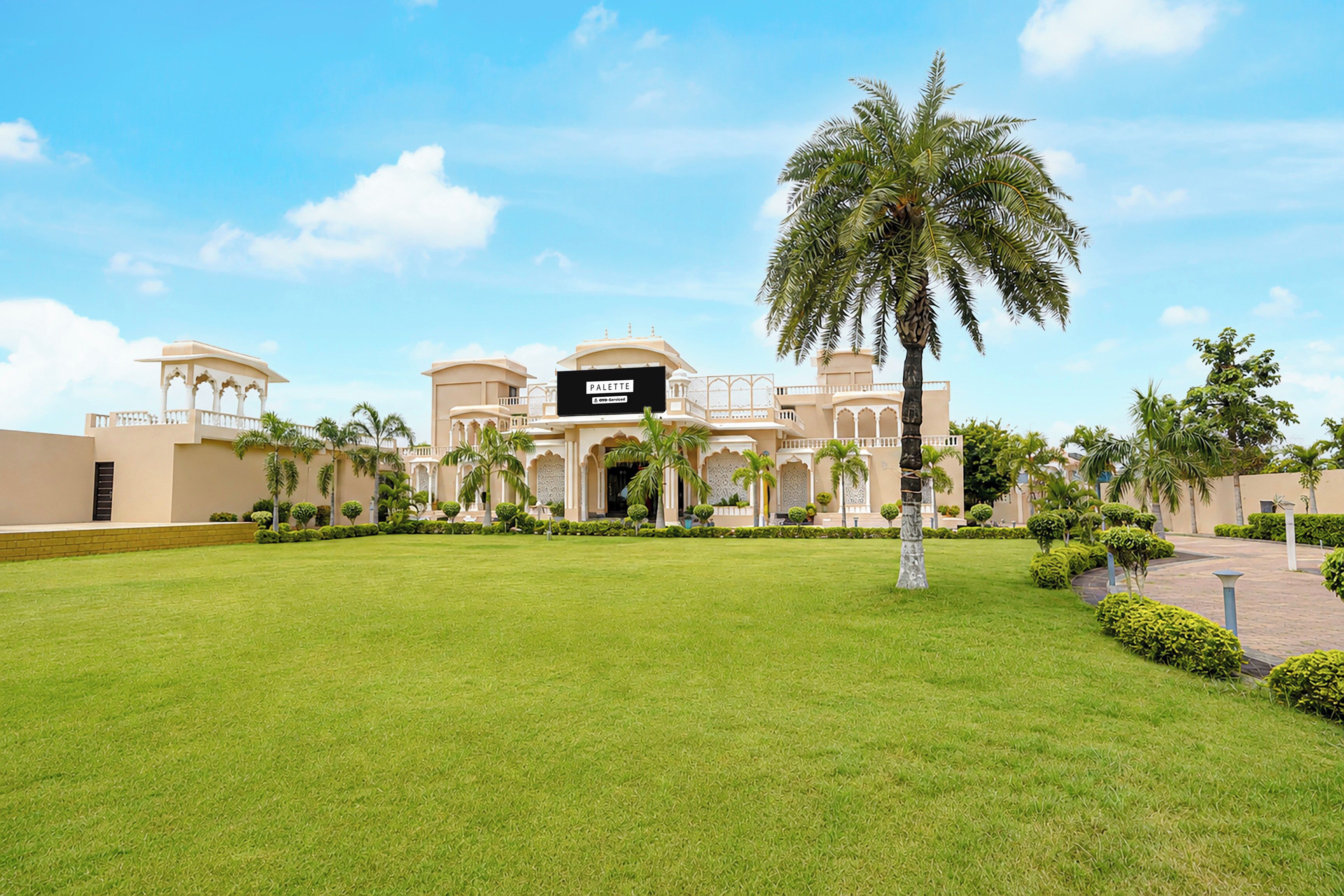 A hotel with a large lawn, palm trees, and a sign reading 'PALETTE & OYO-Serviced'.