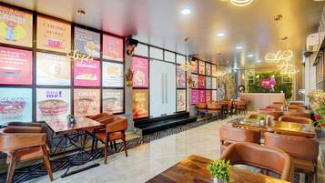 Interior de restaurante con varias mesas y sillas, una variedad de carteles de menú coloridos en las paredes y un diseño de techo moderno.