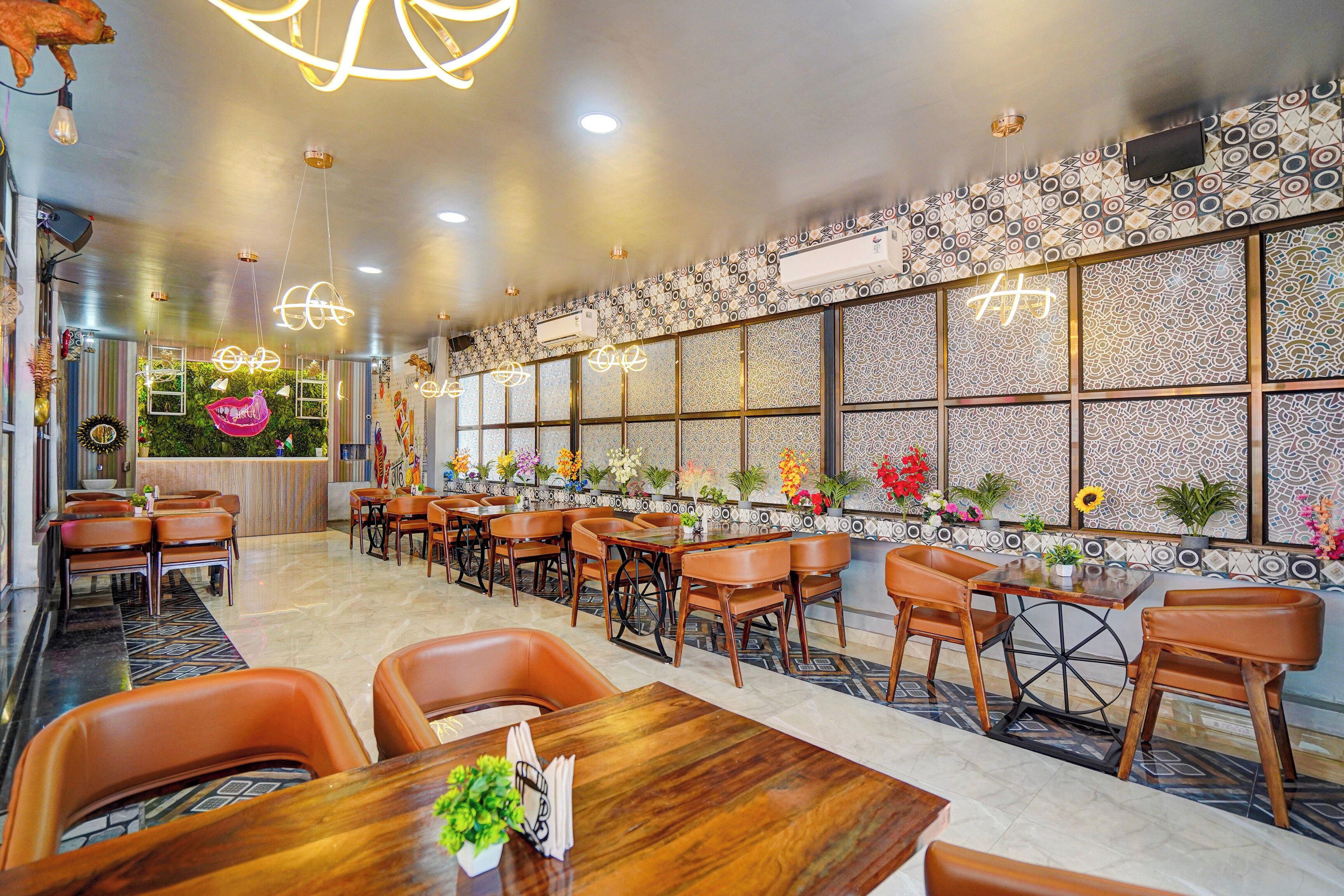 A restaurant interior with multiple dining tables and chairs, decorative wall patterns, and hanging light fixtures.