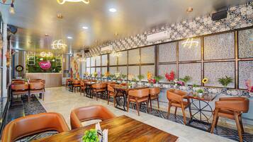 A restaurant interior with multiple dining tables and chairs, decorative wall patterns, and hanging light fixtures.