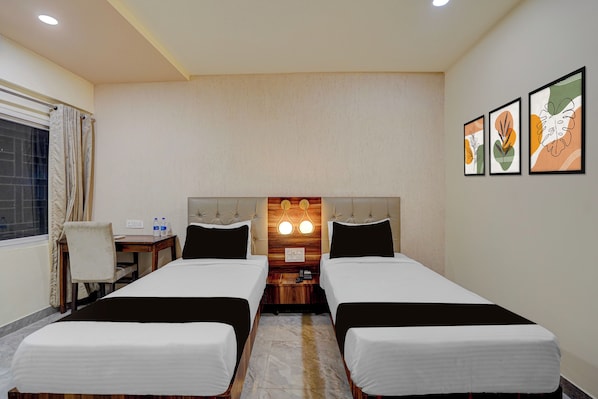 A hotel room with two beds, a desk, a chair, and a window with curtains.