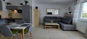 A modern kitchen with a dining area, a grey sofa, and a small table with flowers. - Elegant Vacation Rental “Apartamenty-plaza” – 300 m from the beach, Kolberg (Kołobrzeg)