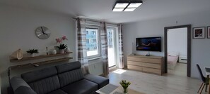 A modern living room with a sofa, a flat-screen TV, and a window with curtains. - Elegant Vacation Rental “Apartamenty-plaza” – 300 m from the beach, Kolberg (Kołobrzeg)