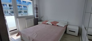 A bedroom with a bed, bedside tables, a radiator, and a window with a view of a building. - Elegant Vacation Rental “Apartamenty-plaza” – 300 m from the beach, Kolberg (Kołobrzeg)