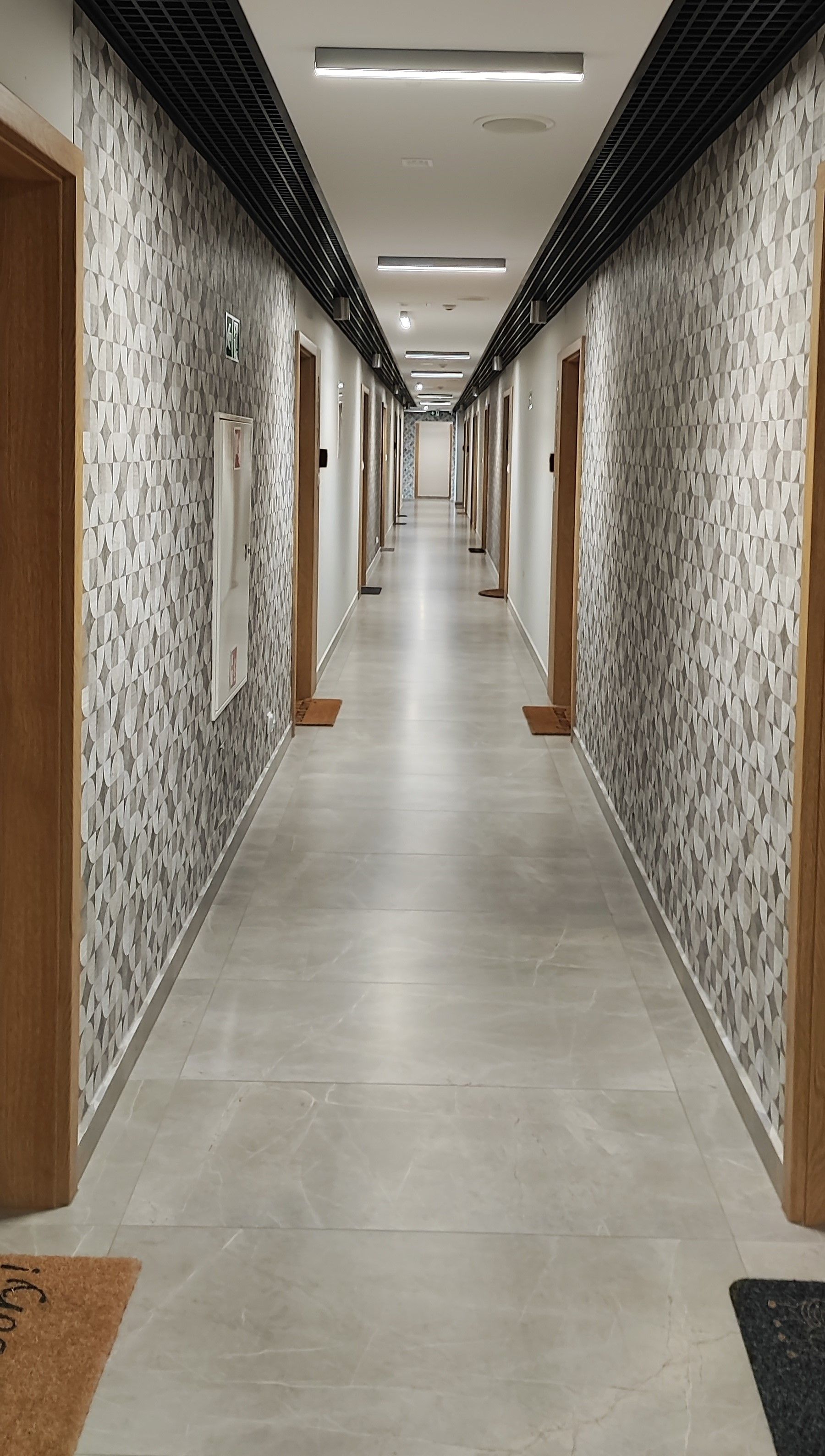 A long, narrow hallway with patterned walls and doors, leading to a bright, well-lit area.