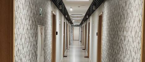 A long, narrow hallway with patterned walls and doors, leading to a bright, well-lit area.