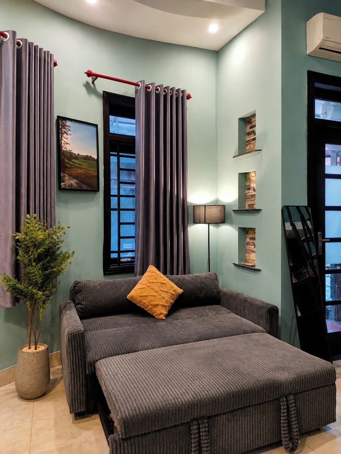 Ein Zimmer mit einer Sofagarnitur, einer Topfpflanze, einem Bild an der Wand und einer Tür mit Blick.