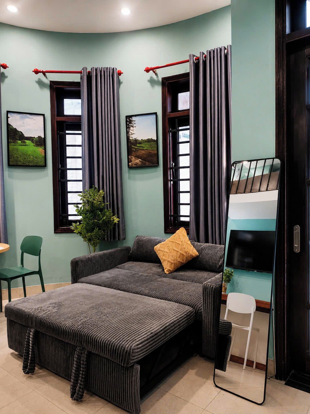 Una habitación con sofá, una mesita, una silla, una cama litera y dos ventanas con cortinas.