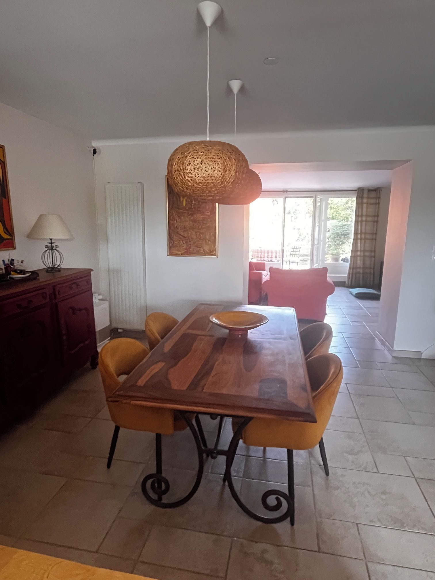 A dining area with a wooden table and chairs, a hanging light fixture, and a view to an outdoor seating area.