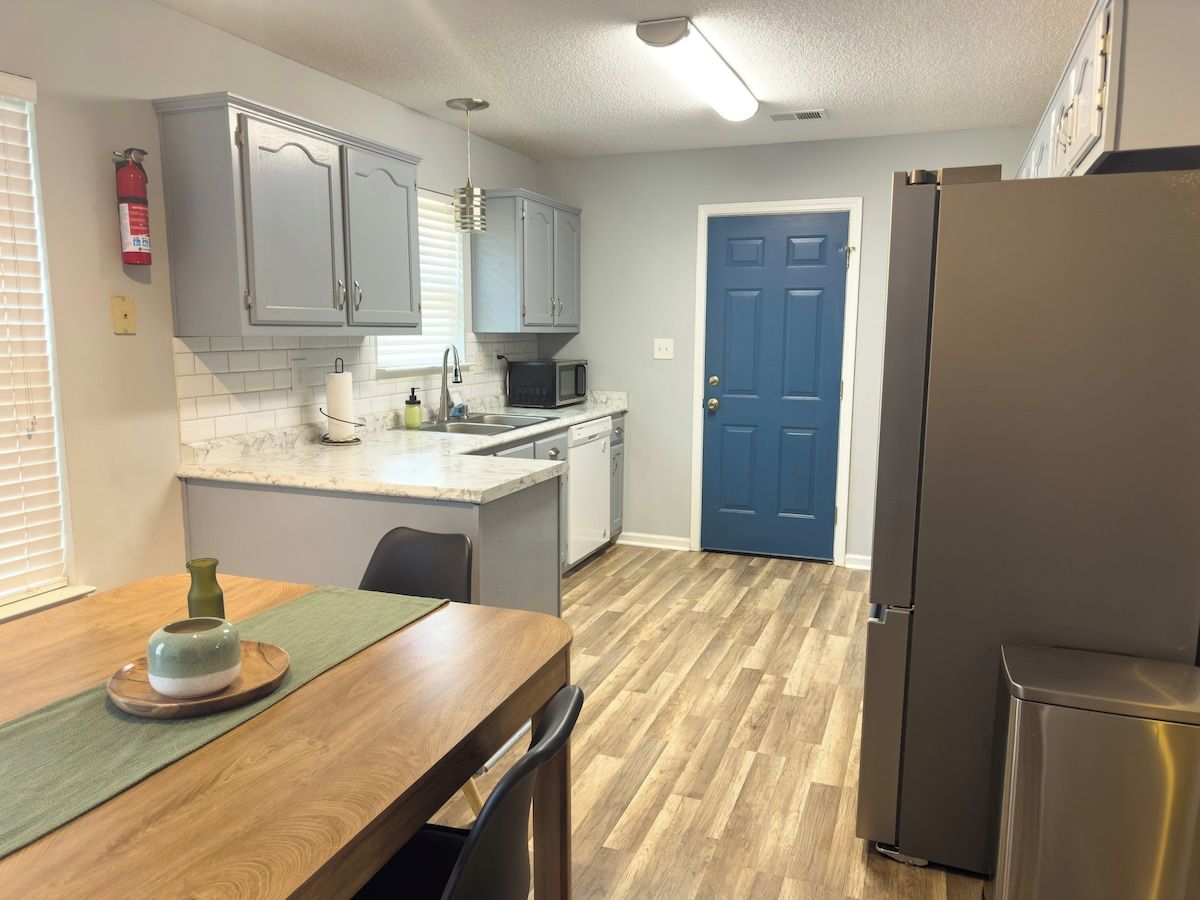 A compact kitchen with grey cabinets, a microwave, a refrigerator, and a dining table with a green placemat.