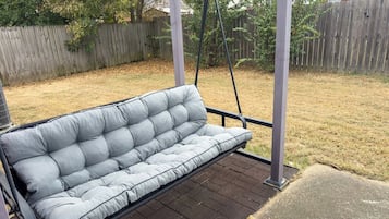 A gray outdoor sofa on a wooden deck with a swing.