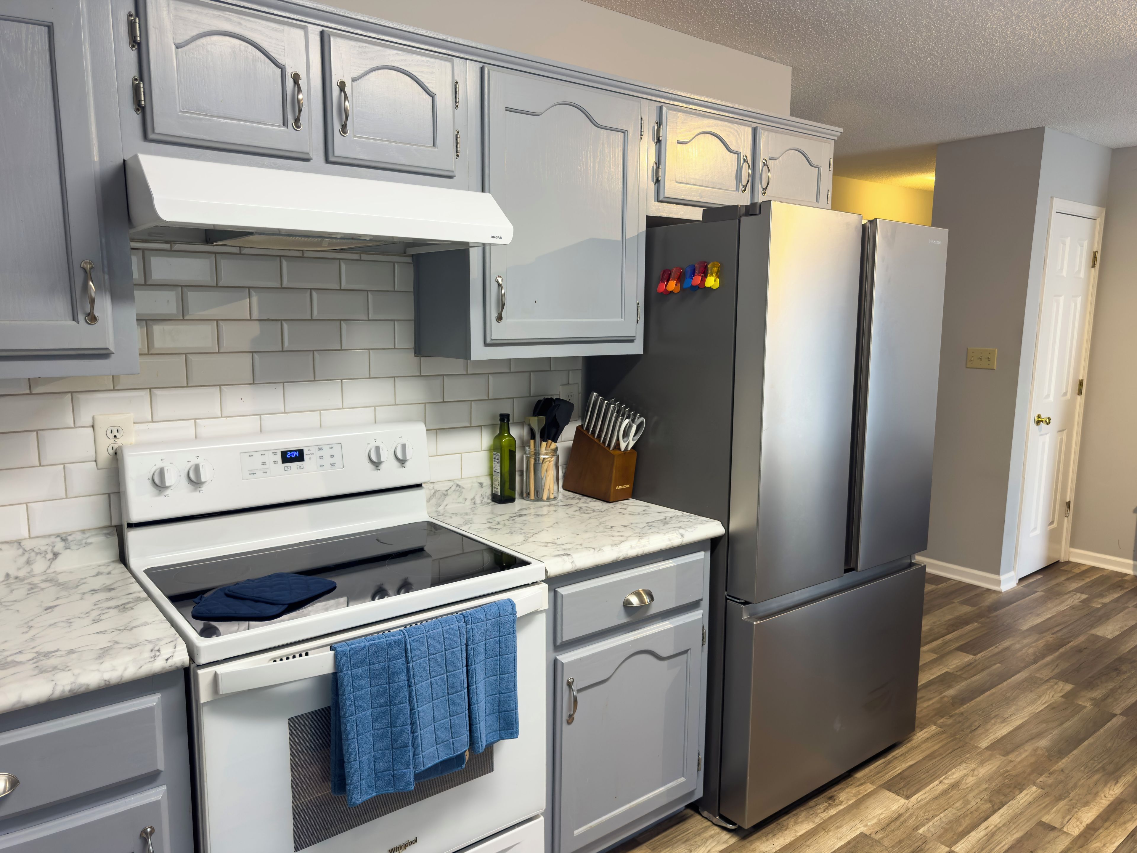 A kitchen with white cabinets, a stainless steel refrigerator, a white stove, and a marble countertop.