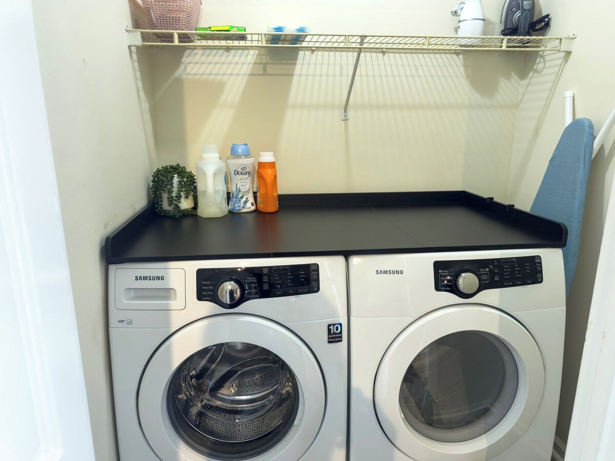 Dos lavadoras Samsung de carga frontal en un cuarto de lavado, con un estante superior que contiene varios objetos.