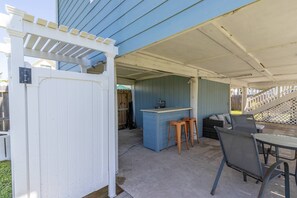 Ein überdachter Patio-Bereich mit einer weißen Pergola, einer blauen Wand und einer Bar mit Hockstühlen.