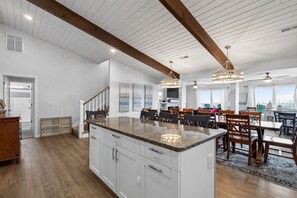 Een ruime keuken met een groot schiereiland, houten balken in het plafond en een eethoek met stoelen en een tafel.