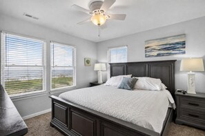 A bedroom with a bed, two bedside tables, a ceiling fan, and large windows. - Healing Breezes | Oceanfront • Private Pool • 7BR Luxury Retreat (Virginia Beach)