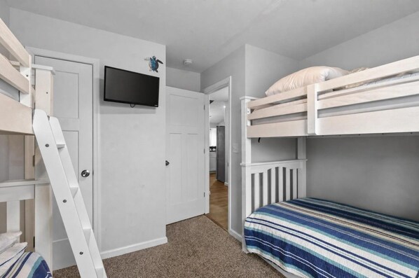 Ein Zimmer mit Etagenbetten, einem an der Wand befestigten Fernseher und einer Leitern.