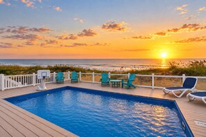 A pool area with a view of the ocean at sunset, deck chairs, and a basketball hoop. - Healing Breezes | Oceanfront • Private Pool • 7BR Luxury Retreat (Virginia Beach)