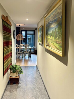 Een gang met een eethoek, een groot schilderij en een wanddecoratie met een structuur.