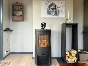 Een moderne woonkamer met een houtkachel, een open haard, een wandplank met decoratieve objecten, en een ingelijst beeld boven de kachel.