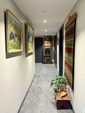 A hallway with framed paintings, a decorative cabinet, and a woven tapestry.