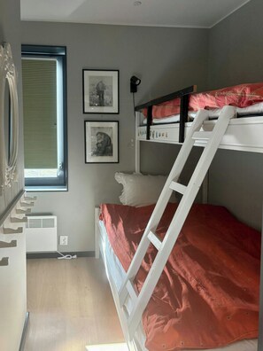 Een slaapkamer met een stapelbed, een raam met jaloezieën en twee ingelijste foto's aan de muur.