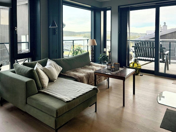 A modern living room with a green sofa, a coffee table, and a view of a balcony with outdoor furniture.