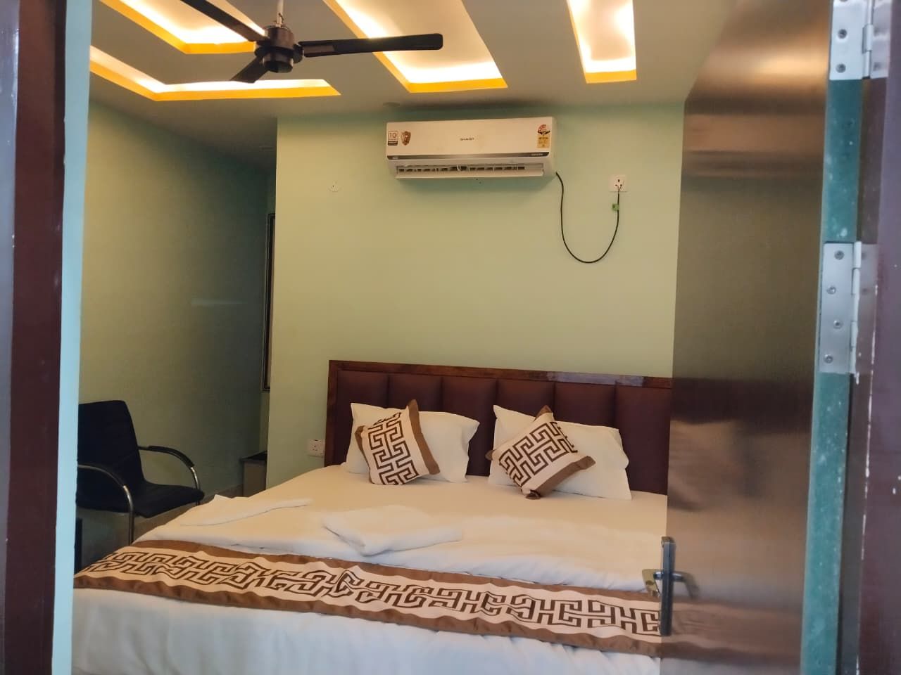 Una habitación de hotel con una cama, ventilador de techo, aire acondicionado y una silla.