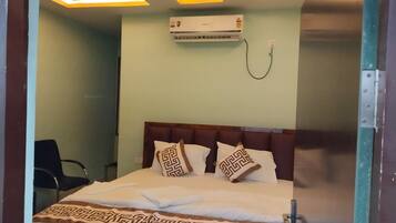 Una habitación de hotel con una cama, ventilador de techo, aire acondicionado y una silla.