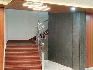 Una escalera con escalones de madera y barandillas de metal, que conduce a una plataforma con pared de textura oscura.