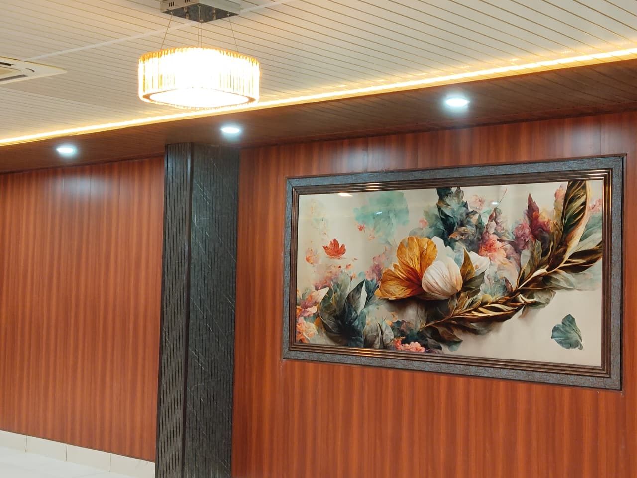 Una obra de arte floral en marco sobre una pared de madera, con una lámpara moderna colgante.