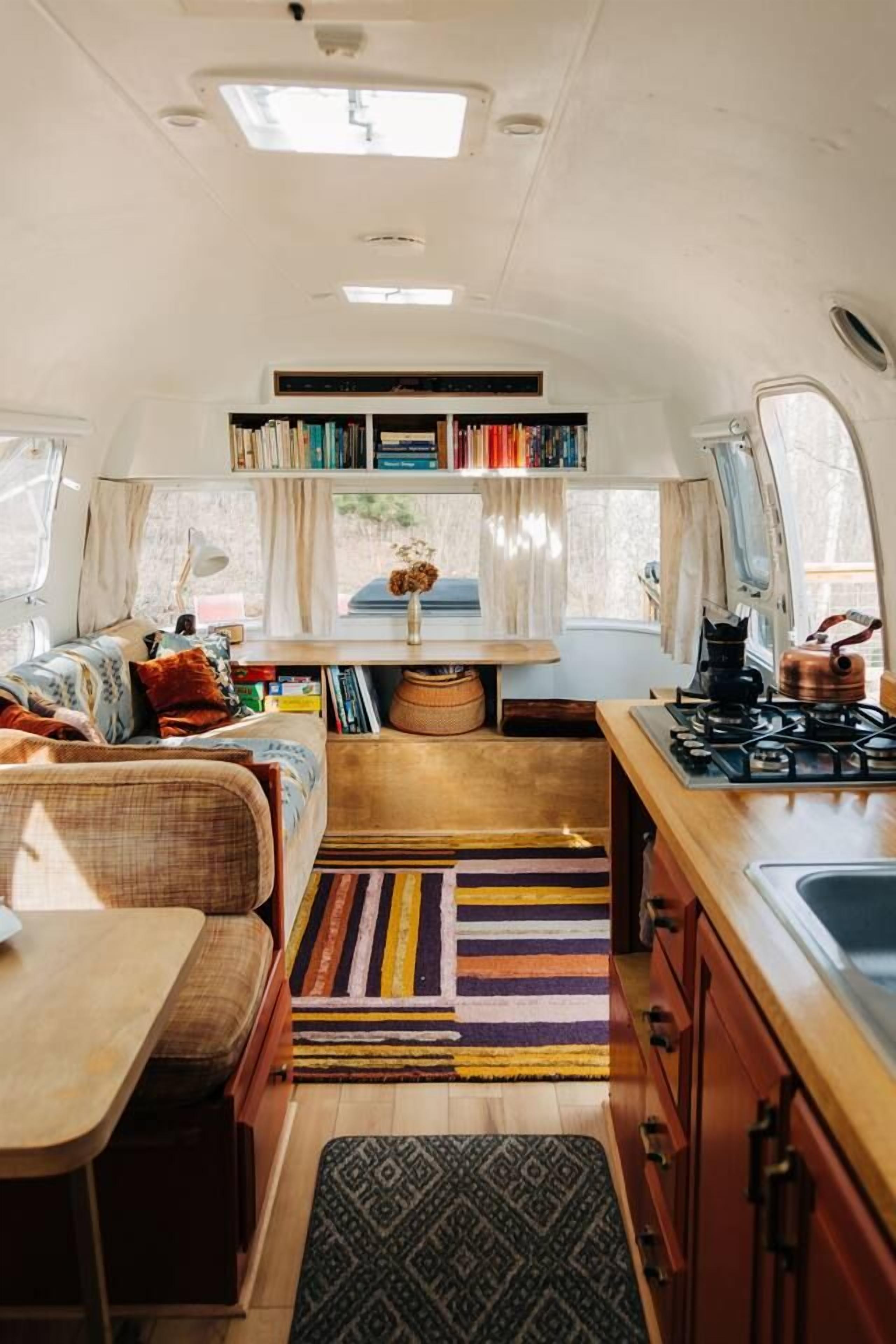 A compact RV interior with a kitchenette, a seating area, and a bookshelf.