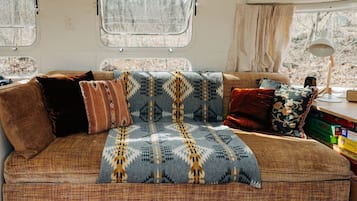 Een gezellig interieur van een camper, met een bank, kussens en een plaid.